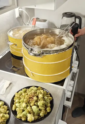 Two beer kettles on a stove boiling vigoriously with immersion heaters